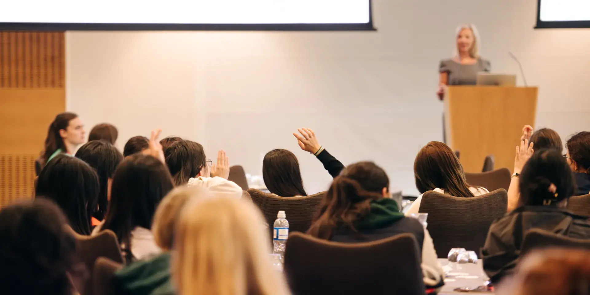 Students in lecture, facing teacher who is standing at the front of the room
