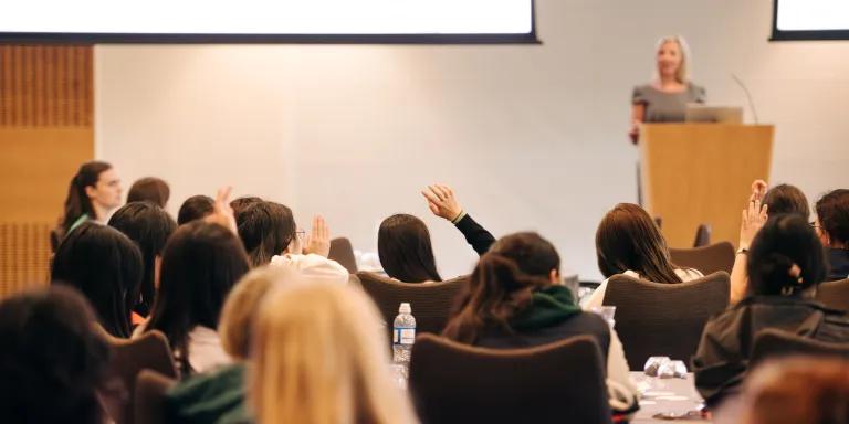 Students in lecture, facing teacher who is standing at the front of the room