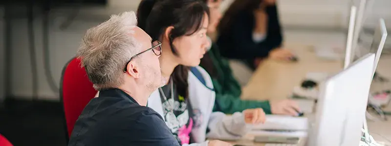 Male teacher advising students on their computers, in a classroom