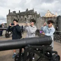 Three male students at Stirling castle, taking photos beside a cannon