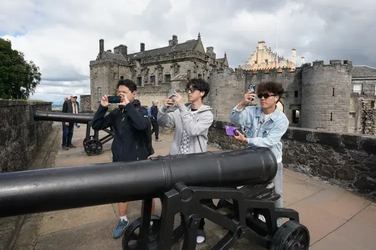 Three male students at Stirling castle, taking photos beside a cannon