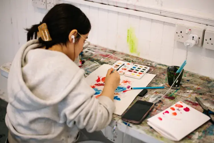 Student sitting down painting on our Design course